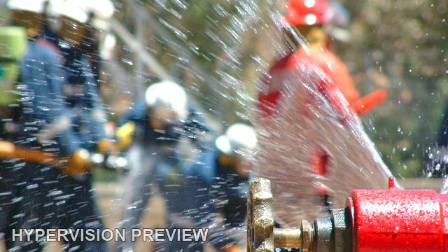 Red Hydrant with Fire Crew Behind Water Spray