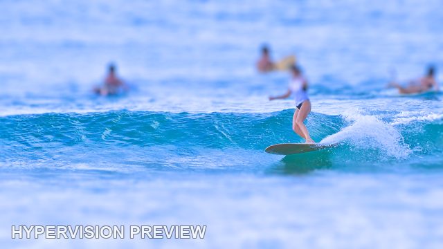 Longboarder with Surfers Waiting Beyond — Cool Blue / Selective Focus