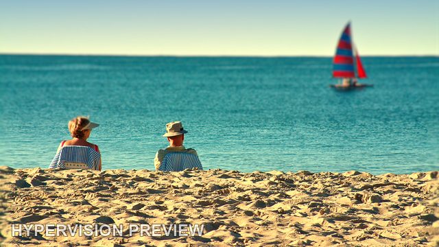Two Beachgoers Watching a Small Sailboat — Selective Focus Edit