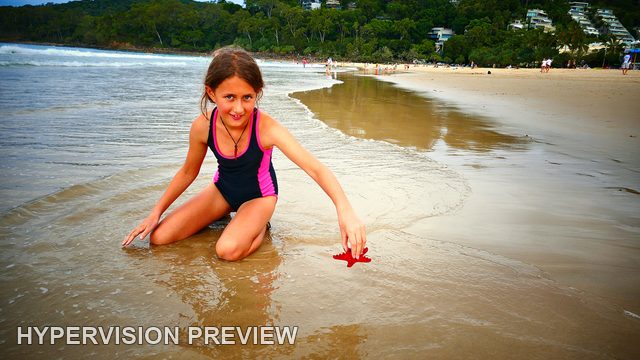 Child Kneeling with a Red Object Beside the Water